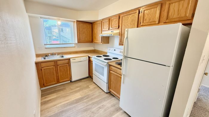 Charming, bright kitchen with warm wooden cabinets, modern appliances, and inviting laminate wood flooring, ideal for creating culinary delights.