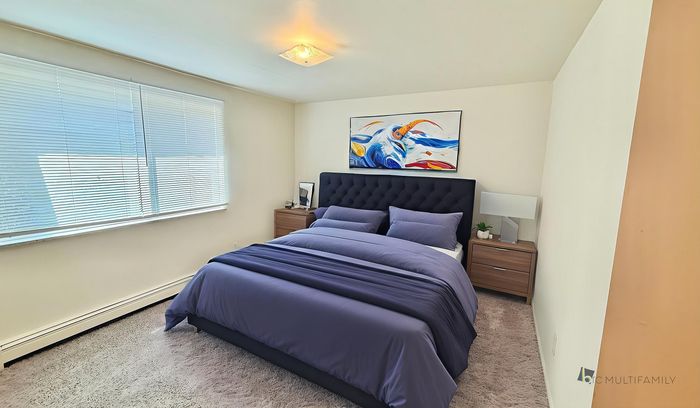 Bright and cozy bedroom featuring a plush bed with navy bedding, elegant side tables, and captivating modern artwork, enhanced by natural light from large windows.