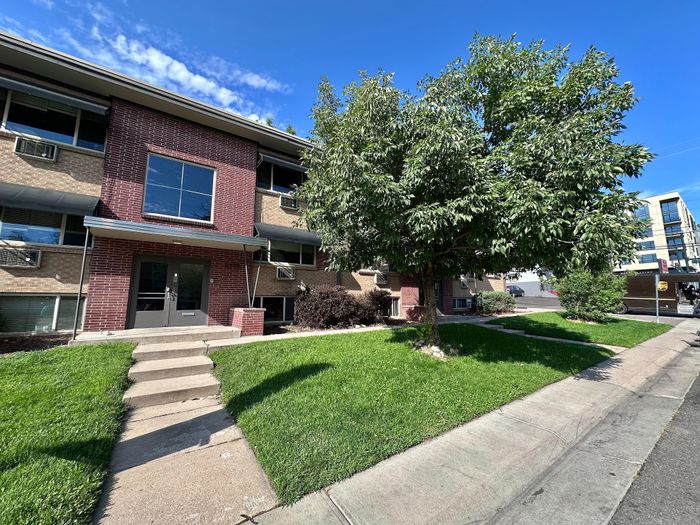 Charming apartment building with a classic brick facade and lush green landscaping, featuring a welcoming entrance and ample natural light.
