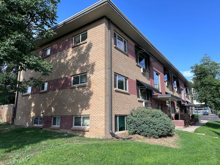 Charming brick apartment building with lush greenery and a welcoming entrance, perfect for urban living.