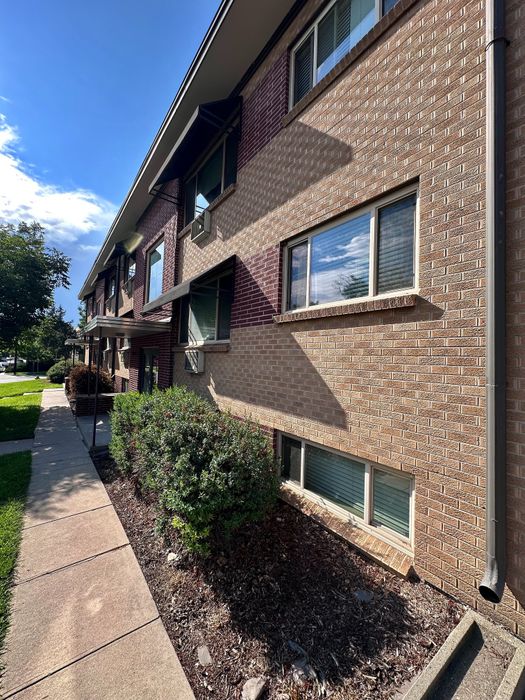 Charming brick apartment building with well-maintained landscaping and large windows, basking in beautiful sunlight.