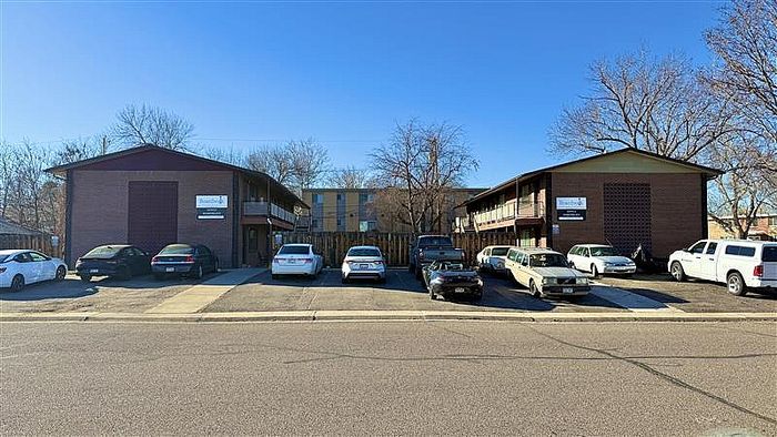 Charming brick apartment complex with ample parking, surrounded by trees for a serene living environment.