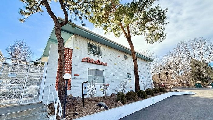 Charming white apartment building with unique exterior, surrounded by lush greenery and a spacious driveway.