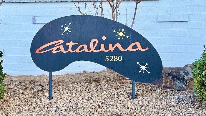 Chic and inviting apartment sign reading 'Catalina 5280' with decorative graphic accents, set amidst a serene stone landscape.
