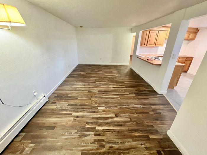 Bright and inviting open-concept living area with stylish wood flooring and a peek into a modern kitchen with wooden cabinetry.