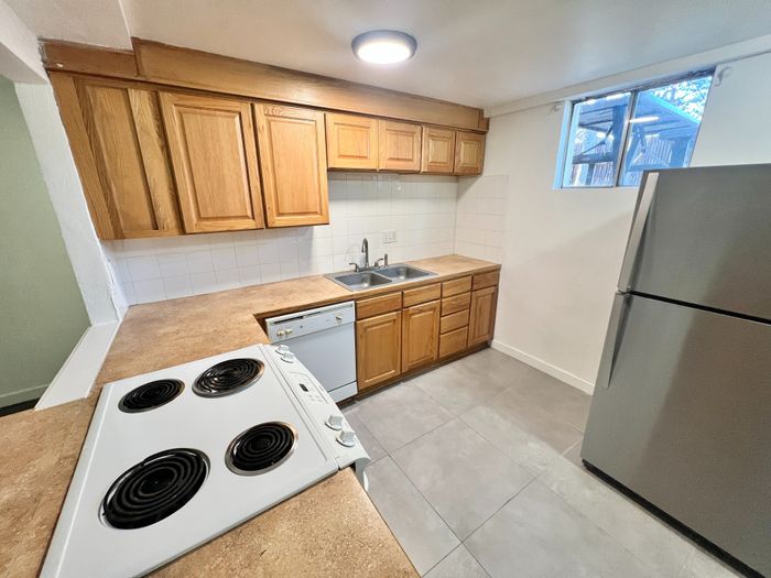 Inviting kitchen with sleek appliances, warm wooden cabinetry, and ample countertop space, bathed in natural light from a charming window view.