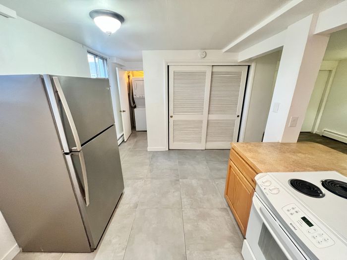 Modern kitchen with sleek stainless steel refrigerator, stylish countertops, and convenient in-unit laundry setup.