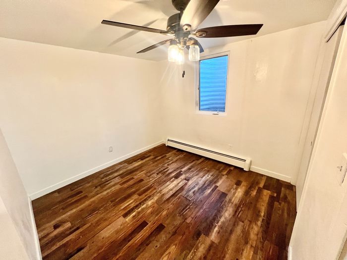 Bright and cozy bedroom with elegant hardwood flooring and modern ceiling fan, perfect for relaxation.