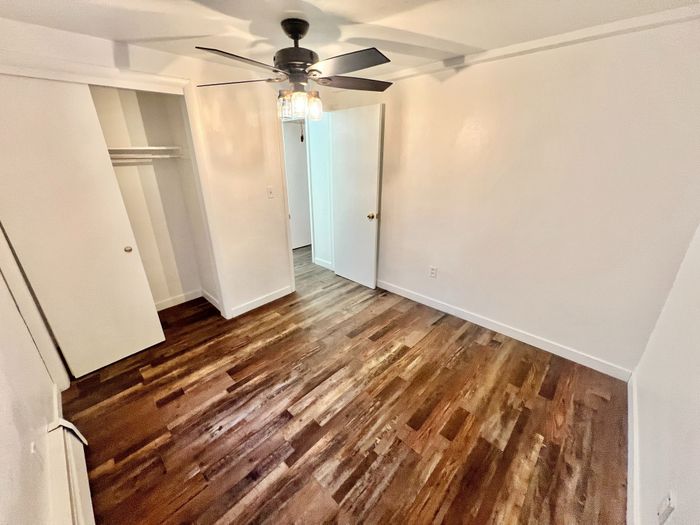 Elegant room with warm wooden floors, modern ceiling fan, and spacious closet, offering a cozy and inviting atmosphere.