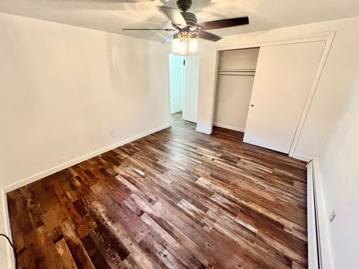Chic bedroom with elegant wood flooring, modern ceiling fan, and ample closet space, creating a cozy and inviting atmosphere.
