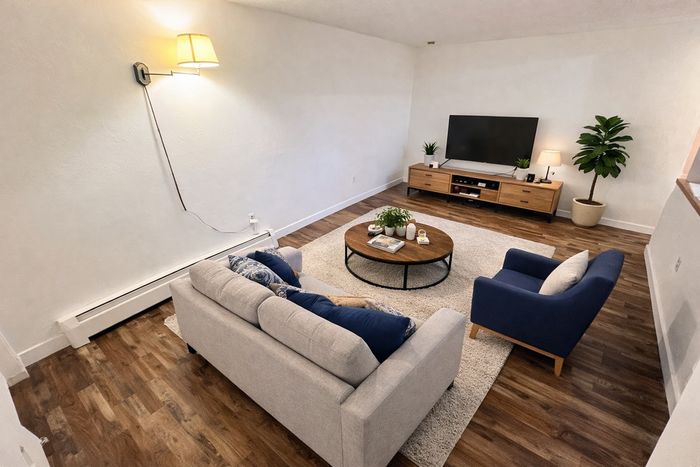 Contemporary living room with stylish decor, featuring a cozy gray sofa, elegant blue armchair, and sleek wooden furniture on polished hardwood floors.
