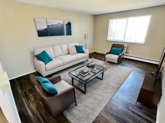 Chic living room featuring a plush white sofa, elegant glass coffee table, and stylish armchairs with teal accents, inviting natural light through large windows.