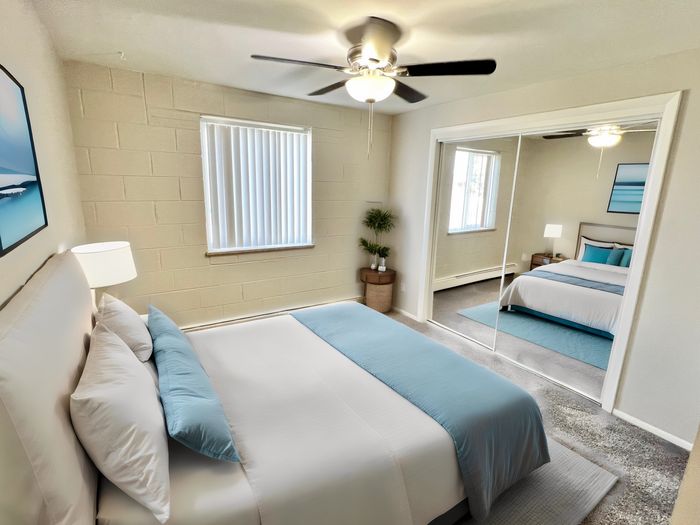 Bright and cozy bedroom with elegant decor, featuring a plush bed, modern ceiling fan, and mirrored closet doors enhancing the space.