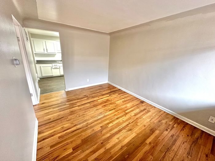 Bright room with elegant wood flooring and a view into a modern kitchen with white cabinetry.