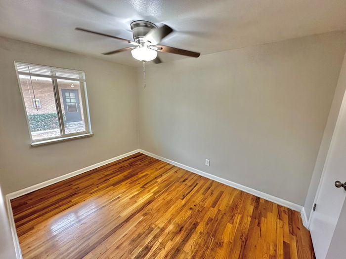 Bright room with polished wood floors, neutral gray walls, and a large window allowing natural light.
