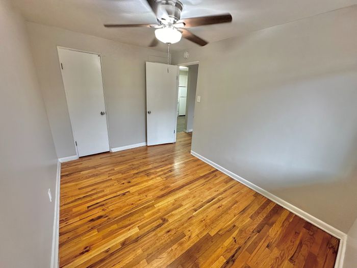 Bright and inviting bedroom with gleaming hardwood floors, modern ceiling fan, and ample closet space.