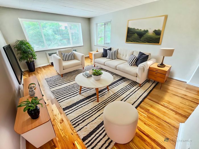 Chic and inviting living room with elegant decor, featuring a plush sofa, stylish striped rug, and abundant natural light from large windows overlooking greenery.