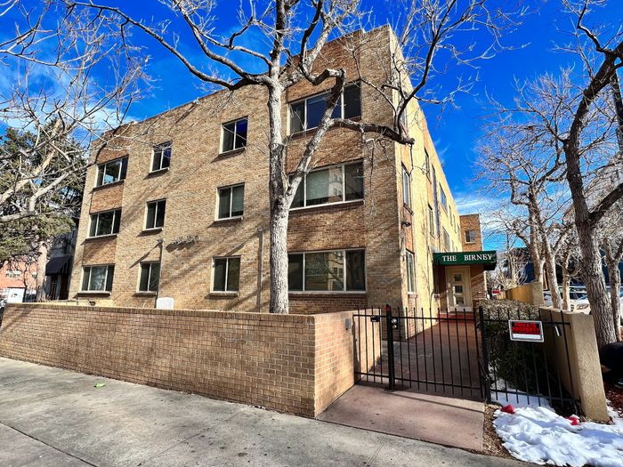 Charming brick apartment building under a vibrant blue sky, featuring gated entry and inviting surroundings at The Birney.
