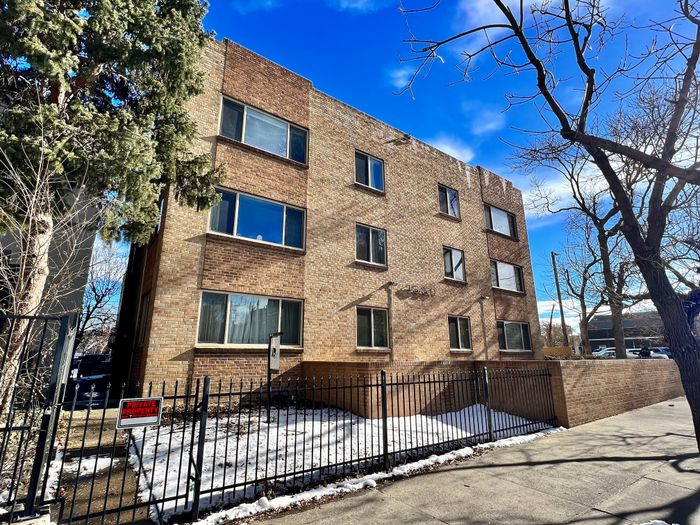 Charming brick apartment building with large windows, surrounded by trees, offering a cozy and inviting urban living experience.