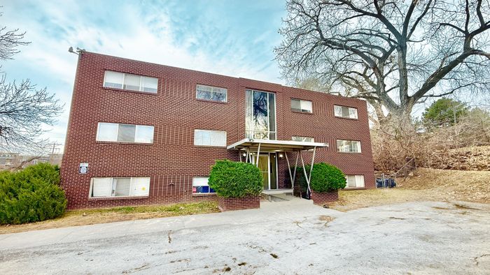 Charming three-story brick apartment building with lush greenery and modern entryway, nestled in a serene suburban setting.