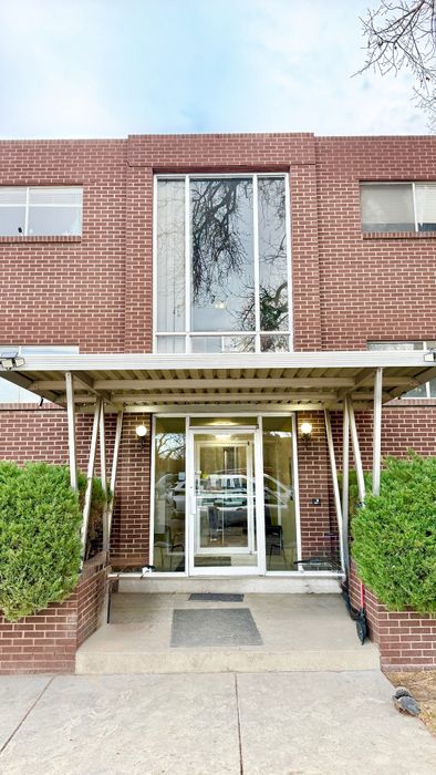 Charming brick apartment entrance showcasing modern design with large windows and inviting greenery.