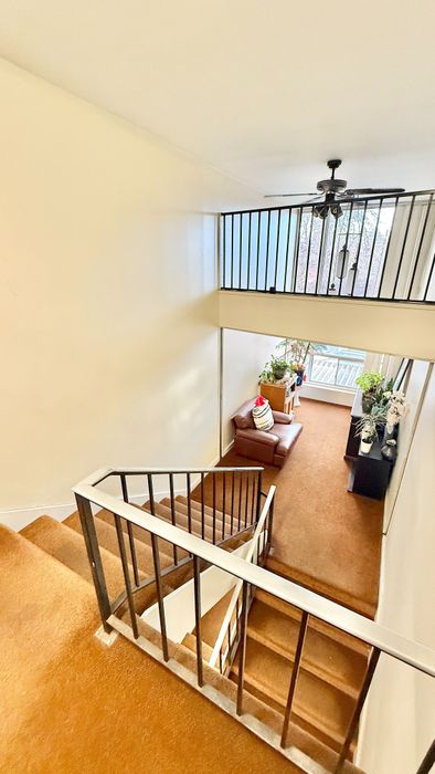 Bright staircase view with elegant railing, cozy seating area, and lush plants beneath a ceiling fan, creating a welcoming ambiance.