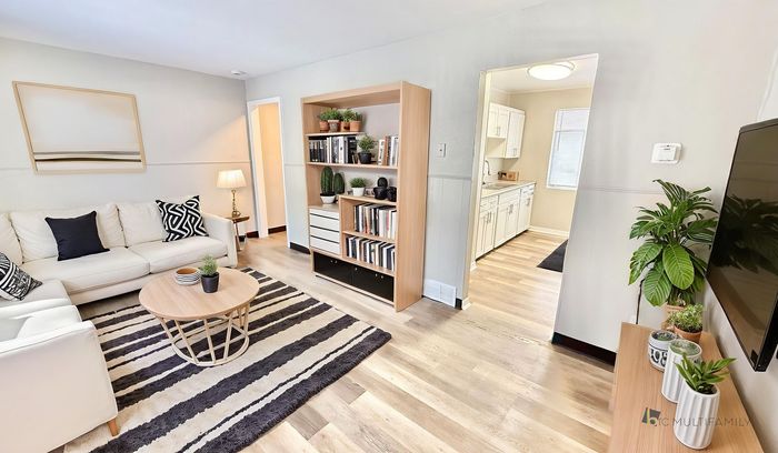 Inviting modern living room with cozy white sofa, chic black and white decor, and elegant wooden shelves; seamlessly connects to a bright kitchen with ample cabinetry.