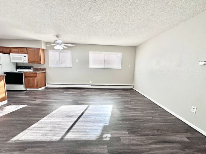 Bright and inviting open-plan living area with sleek wooden flooring and a modern kitchen with wood cabinets, perfect for entertaining.