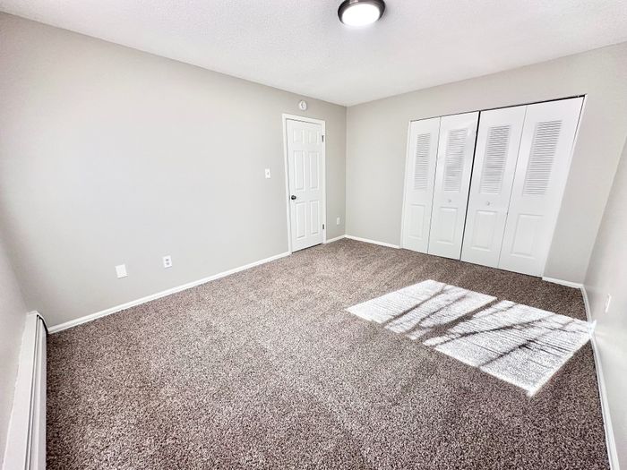 Spacious bedroom with plush carpeting, ample natural light, and large white closet doors for a modern look.
