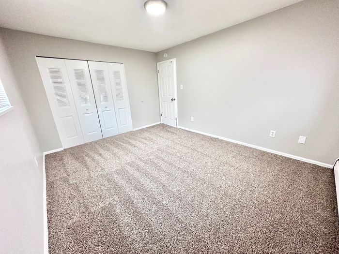 Spacious, sunlit bedroom with plush carpet, ample closet space, and modern neutral tones for a serene atmosphere.