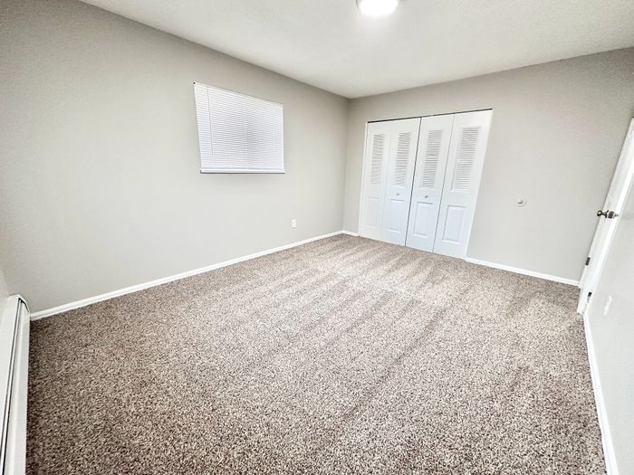 Bright and inviting bedroom with plush carpet, neutral walls, and closet space, perfect for personalization.
