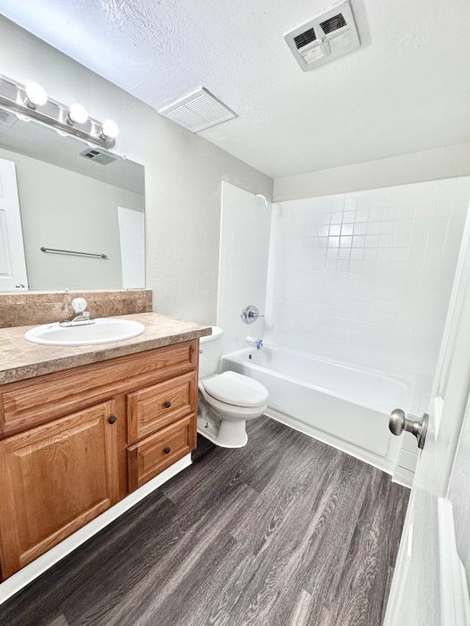Bright and modern bathroom with sleek dark wood flooring, elegant wooden vanity, and pristine white tub and tiles.