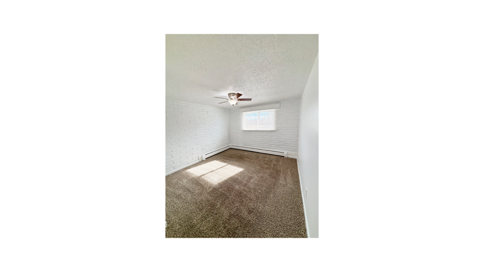 Bright and cozy bedroom with elegant white brick walls, plush carpeting, and a ceiling fan, perfect for a serene retreat.