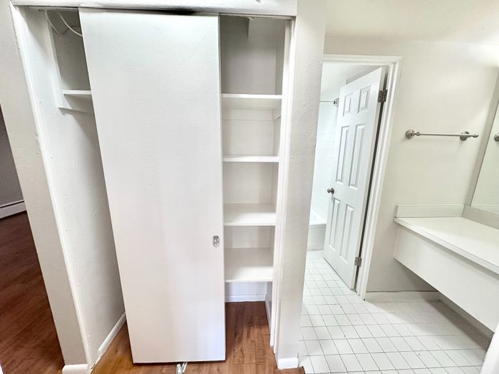 Sleek apartment interior showcasing a stylish closet with sliding doors, leading into a modern bathroom with elegant tile flooring.