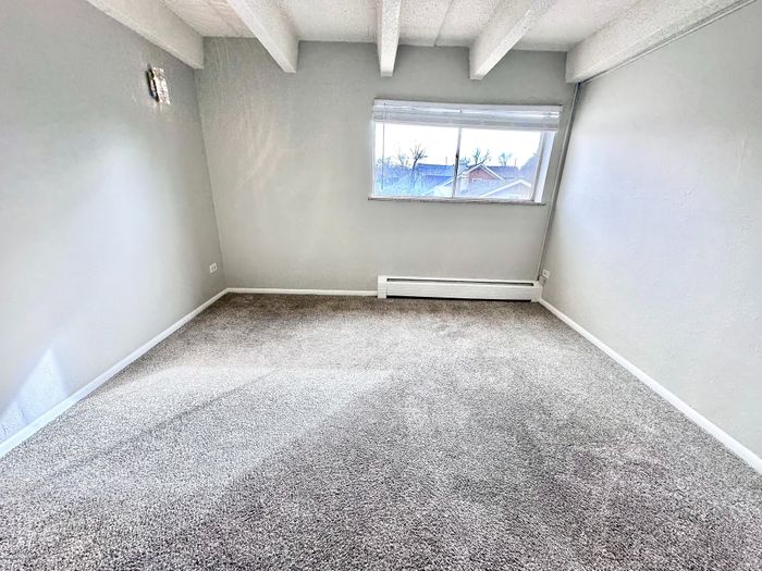 Bright and airy carpeted room with large window, featuring exposed beams and a sleek modern design.