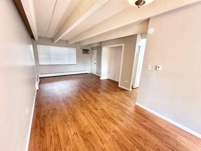 Charming apartment interior featuring elegant wood flooring, inviting neutral walls, and abundant natural light through large window blinds.