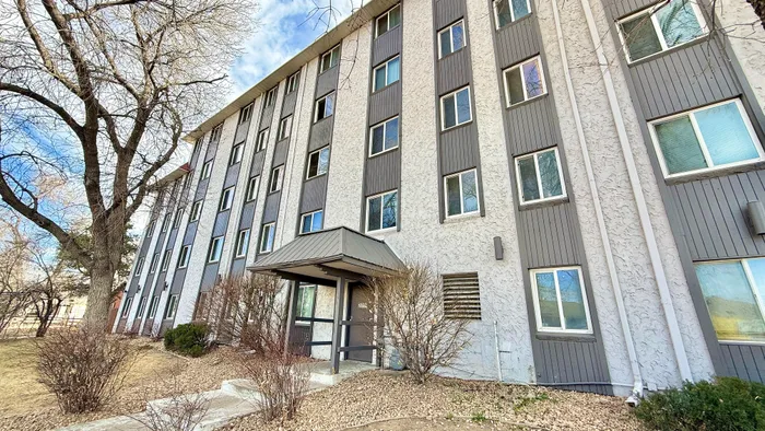 Charming multi-story apartment building with modern gray accents and inviting entrance surrounded by lush landscaping.