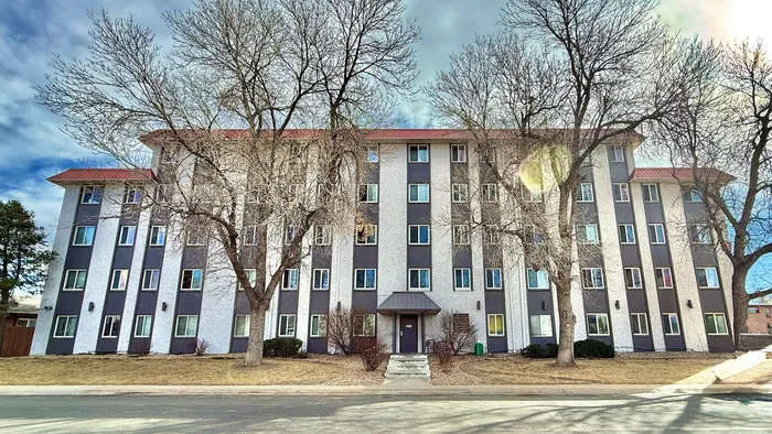 Charming multi-story apartment building with a modern facade and inviting entrance, surrounded by mature trees under a clear sky.