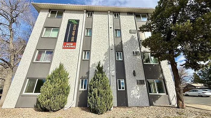 Inviting four-story apartment building with modern exterior and vibrant 'Now Leasing' signage, surrounded by lush greenery and ample natural light.