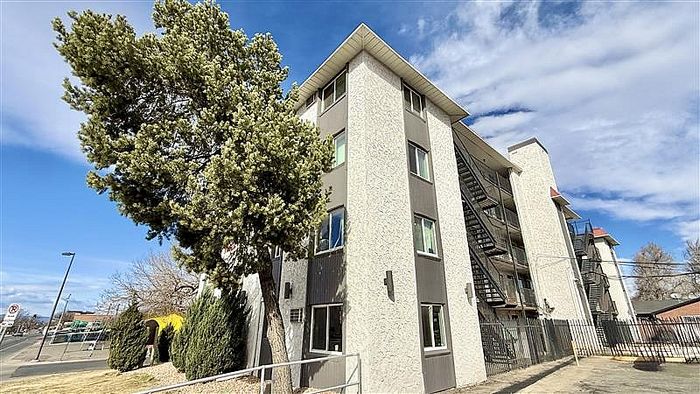 Modern apartment building with textured facade, nestled among lush trees, under a sunny sky.