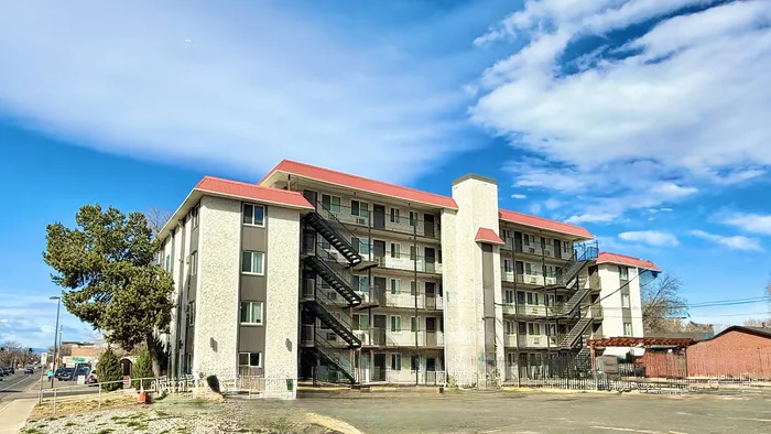 Charming multi-story apartment building with red roofs and open staircases under a vibrant blue sky.