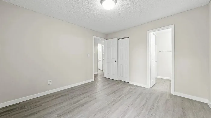 Bright and airy bedroom with sleek wood flooring, ample closet space, and a stylish white interior.