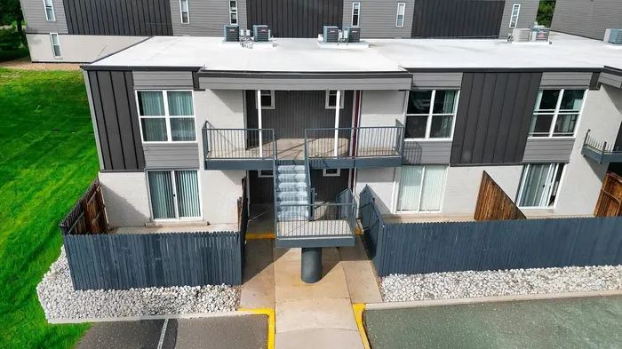 Modern apartment exterior featuring sleek design with balcony, surrounded by well-maintained greenery and secure fencing.