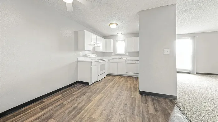 Bright open kitchen with modern white cabinetry and sleek wood flooring, leading to a sunlit living room.