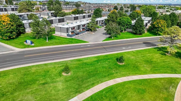 Aerial view of a charming apartment complex nestled among lush greenery, with a scenic road and vibrant community setting.