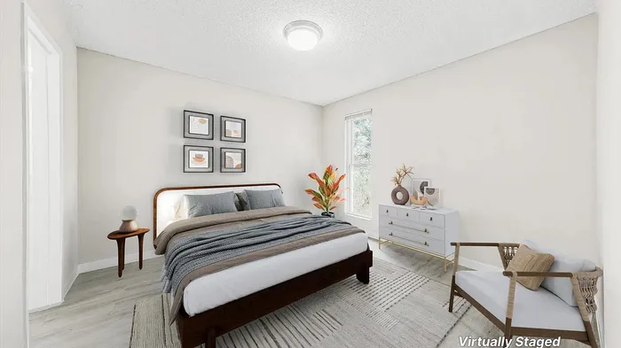 Inviting bedroom with cozy decor, featuring a comfortable bed, modern art, and a large window for natural light, virtually staged.