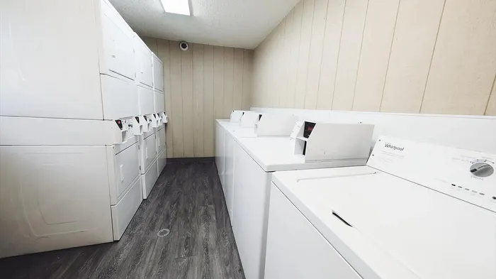 Modern laundry room featuring multiple efficient white washers and dryers, offering convenience and style with sleek wood flooring.