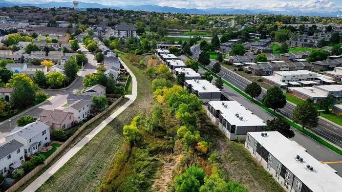 Scenic aerial view of a vibrant suburban neighborhood with lush greenery, winding pathways, and distant mountains, ideal for tranquil living.
