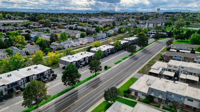 Aerial view of a charming residential neighborhood with tree-lined streets and modern townhouses, offering a picturesque suburban lifestyle with mountain views in the distance.