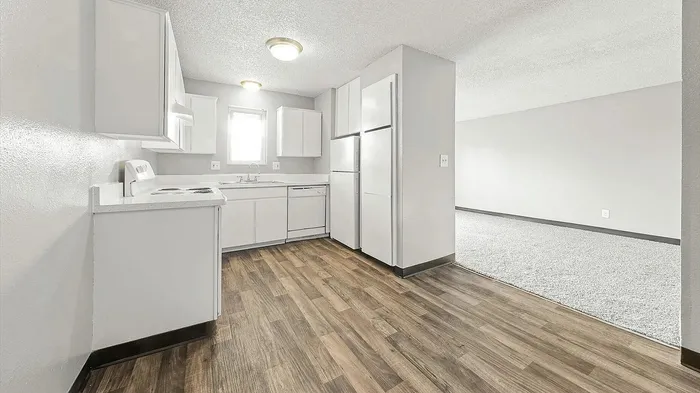 Chic and bright kitchen with sleek white cabinets, modern appliances, and inviting wood flooring leading to a spacious living area.